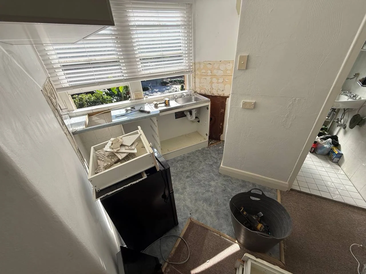 Original kitchen during demolition with removed joinery, exposed plumbing and construction debris